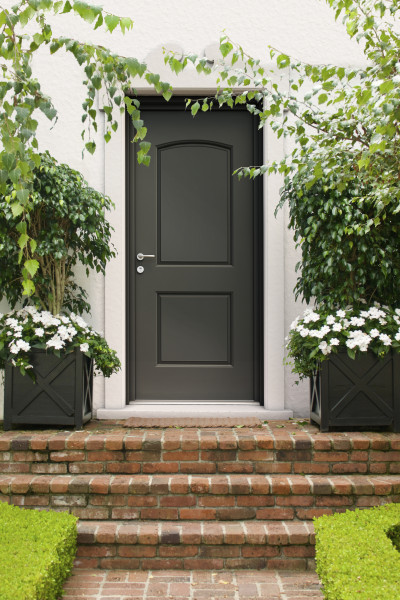 Porte d'entrée acier Boédic - Visuel d'ambiance Extérieur de maison avec escalier en brique, porte d'entrée grise et multiples verdures